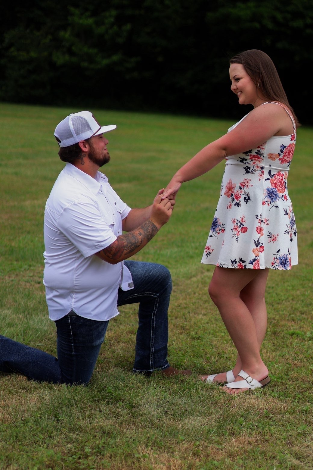 Man on one knee proposing to his partner in a green field