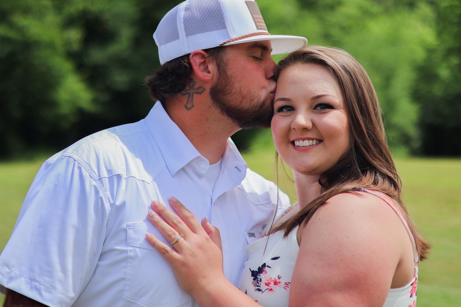 Man kissing his fiancee's temple while she smiles at the camera